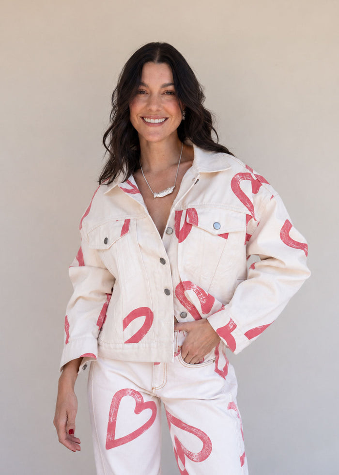 Ivory cotton drill denim jacket with all-over red heart print, front pockets, and barrel sleeves
